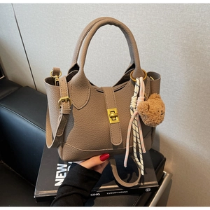 Close-up of khaki litchi grain leather bucket bag with gold buckle and bear charm