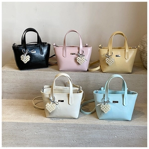Detail view of five pastel PU leather bucket bags with pearl heart charms on stone steps