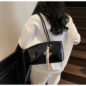 Detail of black glossy hobo bag featuring slim straps and a tennis racket charm on shoulder
