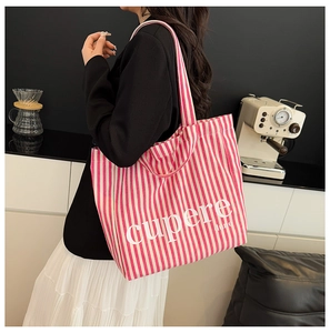 Detail of striped canvas tote bag worn by model in a modern cafe setting