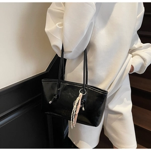 Detail of glossy black underarm bucket bag featuring decorative knotted straps and woven charm