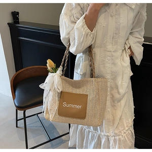 Detail of woven tote bag featuring brown leather patch with Summer text and lace bow charm