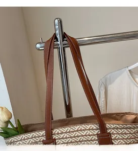 Detail of long brown leather shoulder straps on a woven straw tote bag for women