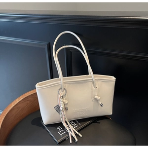 Close-up of white PU leather tote bag with embossed text and colorful tassel on a chair
