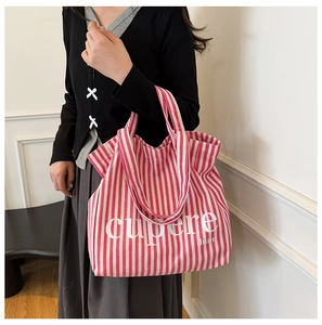 Red and white striped canvas tote bag with letter print worn on shoulder by model
