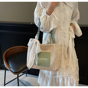 Detail of woven straw tote bag with green accents and large white lace bow decoration