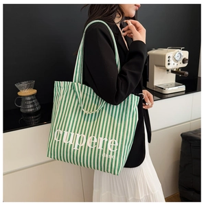 Close-up of a green and white striped canvas tote bag with letter print in a cafe setting