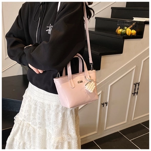 Detail of pink leather bucket bag featuring a metal nameplate and pearl woven pendant charm