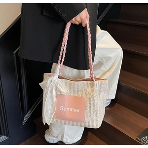 Detail of straw woven tote bag featuring pink handles and a delicate lace bow accent