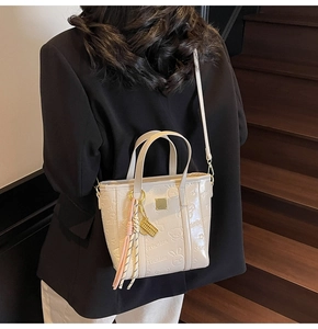 Detail of cream bucket bag with cartoon animal embossing and woven tassel charm