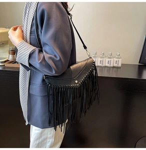 Detailed close-up of a black fringed envelope bag with braided edges and silver buckle