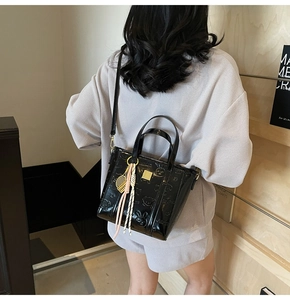 Detail of black embossed patent leather bucket bag with cute cartoon motifs and metallic plate