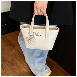 Detail of off-white PU bucket bag featuring a pearl heart charm and metallic logo tag