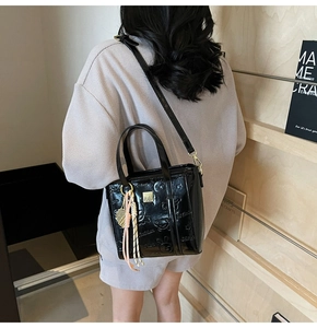 Detail of black patent leather bucket bag with embossed bear and woven charm accessory