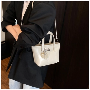 Close-up of cream-white glossy bucket bag with pearl heart charm and shoulder strap