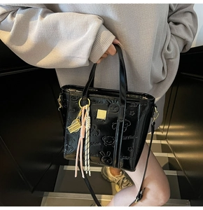Detail of black embossed patent leather bucket bag featuring cute cartoon patterns and hardware