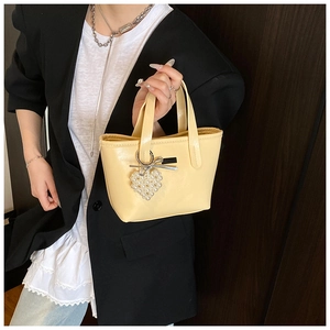 Detail of yellow bucket bag featuring pearl heart charm and silver bow decoration