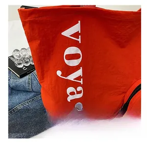 Détail du sac fourre-tout orange en nylon avec imprimé voyage et poche ronde zippée