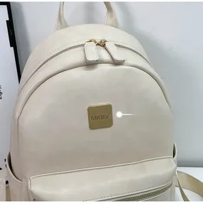 Detail of a minimalist cream-white backpack featuring a gold MKBV metal logo and premium texture