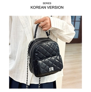 Detail of black quilted backpack featuring diamond patterns and chain strap held by hand