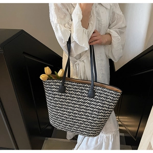 Detail of woven straw tote bag with black and white patterns and yellow tulips inside