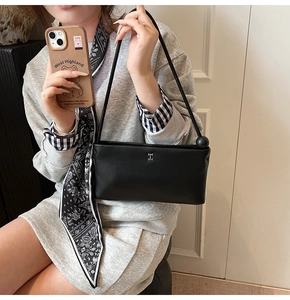 Dettaglio di una borsa squadrata in pelle nera con logo H argento e ciondolo a sfera