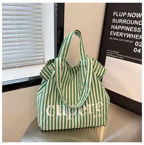 Detailed view of green striped canvas tote bag with Cupere Dune text on metal table
