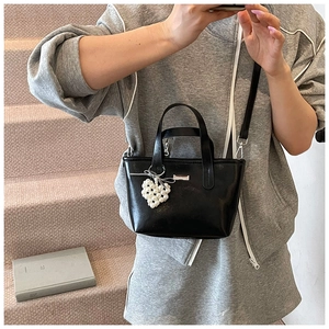 Detailed shot of black patent leather bucket bag with a heart pearl charm and shoulder strap