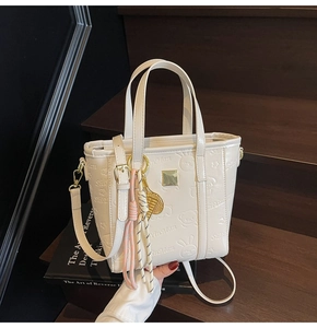 Detail of cream-colored bucket bag with embossed rabbit and bear patterns and gold plaque