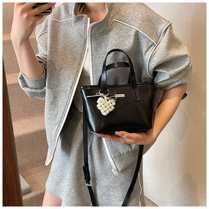 Detail of black mini bucket bag featuring a pearl heart charm and metallic brand logo