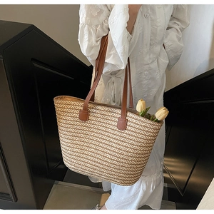 Detail of a large woven straw tote bag with brown leather straps on a fashion model