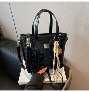 Close-up of black glossy handbag with embossed teddy bear patterns and gold tennis charm