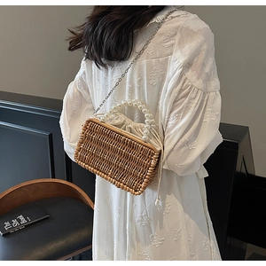 Detail of hand-woven straw bag with elegant pearl handle and metal chain strap