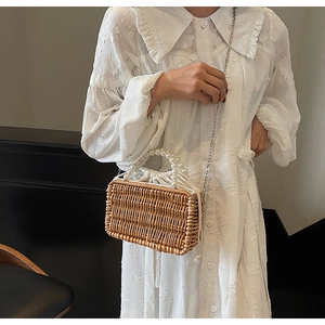 Detail of hand-woven straw bag featuring a pearl top handle and metal chain strap