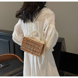Detail of woven straw bag with pearl handle, pearl shoulder strap and drawstring closure