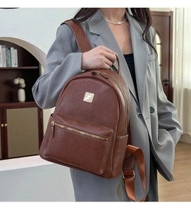 Detail of a brown leather backpack with golden metal logo and functional zippers