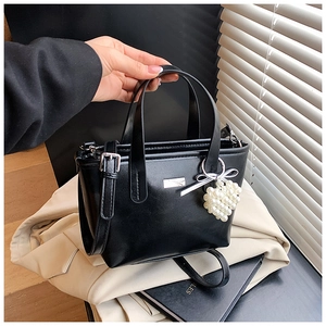 Detail of black glossy leather bucket bag featuring heart pearl charm and silver logo