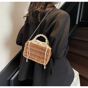 Detail view of woven straw box bag with large pearl handle and silver chain strap