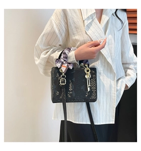 Détail d'un sac à main noir à motif écailles avec foulard déco et pendentif doré