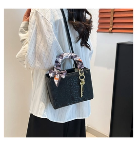 Détail du sac à main noir motif serpent avec foulard en soie décoratif et pendentif doré