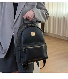 Detail view of stylish black leather backpack showing golden logo plate and metal zipper