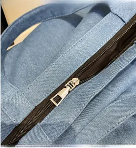 Detailed close-up of smooth silver metal zipper and blue denim fabric on tote bag