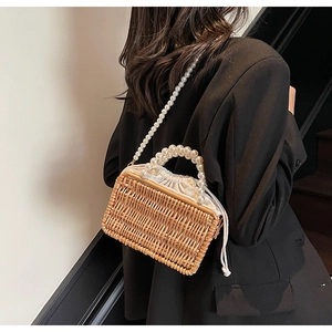 Detail view of woven straw bag featuring elegant pearl handle and pearl crossbody strap