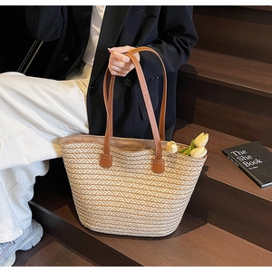 Detail of large straw tote bag featuring brown leather straps and woven wave texture