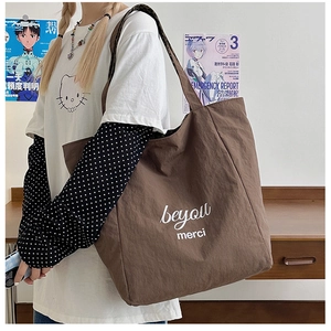 Detail of dark brown tote bag featuring white beyou merci text and textured canvas fabric
