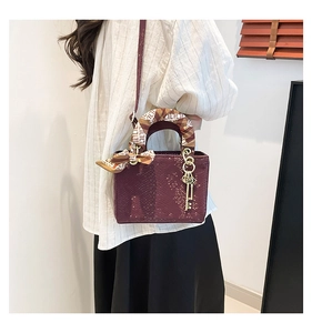 Détail du sac bordeaux à texture d'écailles avec poignée en foulard et pendentif doré