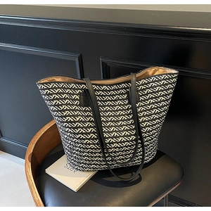 Detail view of woven tote bag showing wavy geometric patterns and black leather straps