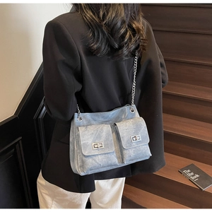 Détail montrant la texture en denim bleu délavé et la bandoulière en chaîne de ce sac fourre-tout