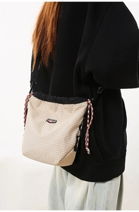 Detail of beige plaid crossbody phone bag with drawstring closure and braided cord accents