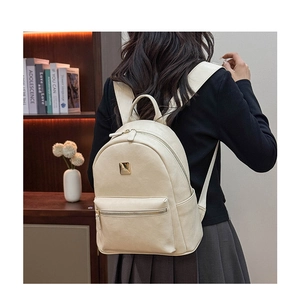 Detailed close-up of a cream faux leather backpack with gold metal logo and front pocket